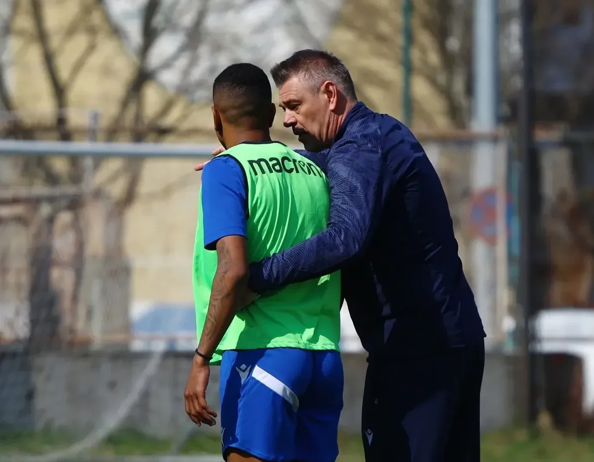 Trener s rukom na ramenu mladog fudbalera koji nosi zeleni prsluk.