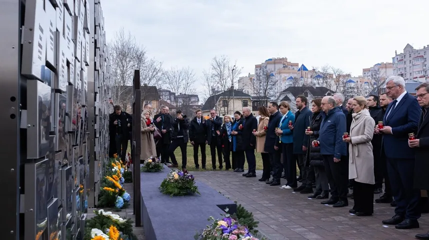 Visoki zvaničnici i drugi učesnici stoje u redu ispred spomen-zida, držeći upaljene svijeće i polažući vijence.
