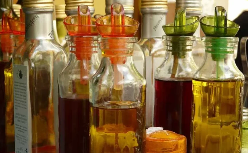 Više staklenih bočica sa raznim vrstama ulja i sirćeta, svaka sa dozatorom za sipanje.