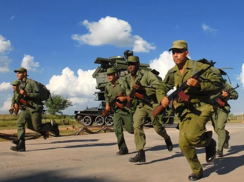 Kubanski vojnici u uniformama trče sa automatskim puškama u ruci, pored vojnog vozila i raketnog lansirnog sistema.