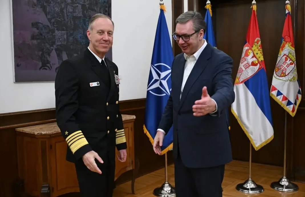 Američki vojni zvaničnik pruža ruku Aleksandru Vučiću ispred zastava NATO-a i Srbije.