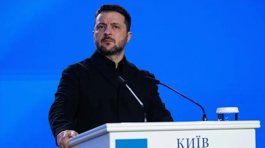 Volodimir Zelenski, predsjednik Ukrajine, u crnom sakou, stoji za podijumom sa mikrofonom i čašom vode.