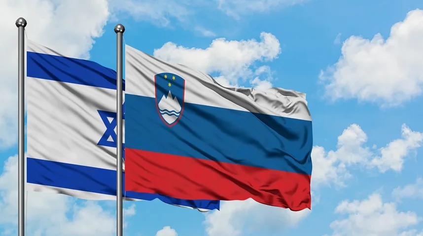 Druga do drugog na vjetru se vijore zastave Izraela i Slovenije, na pozadini neba punog oblaka.