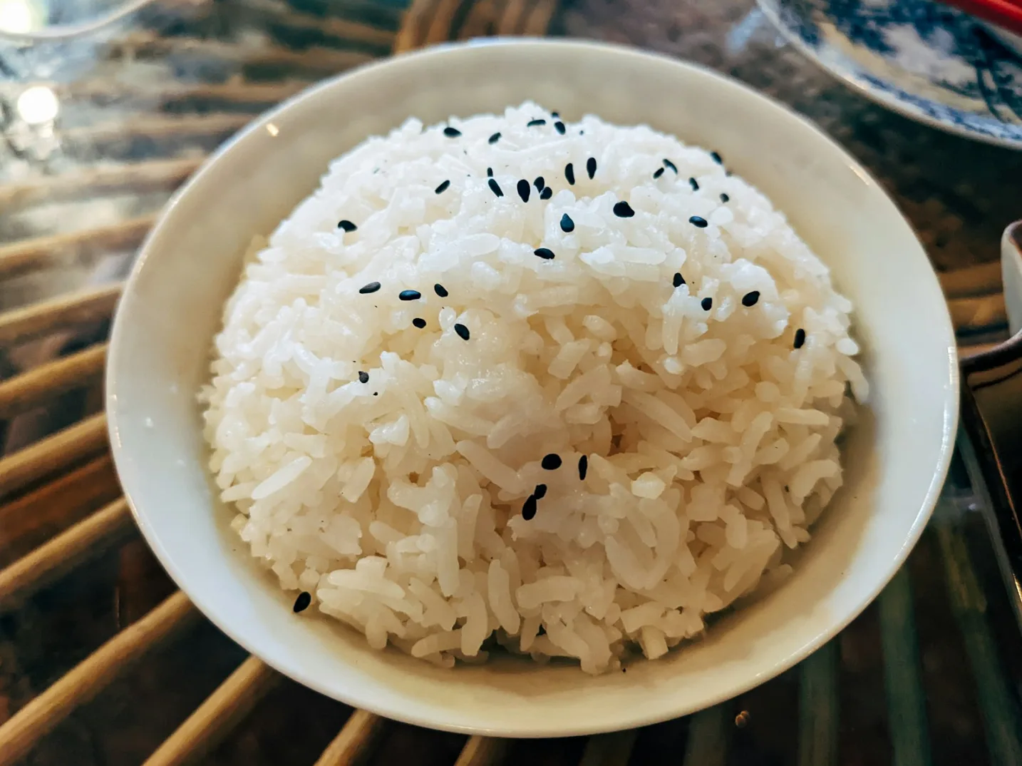 Zdjela svježe skuhane bijele rize posute crnim sjemekama susama, servirana na drvenom podlošku.