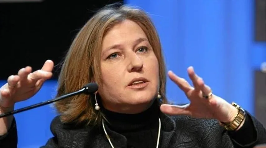 Žena sa plavom pozadinom govori kod mikrofona, sa rukama podignutim u gestikulaciji.