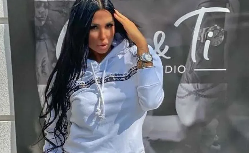 Žena sa dugom crnom kosom, obučena u bijelu Adidas hudicu, pozira sa rukom na glavi.