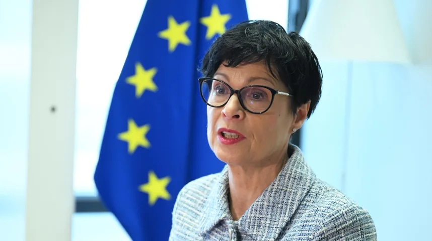 Žena sa naočarima i kratkom crnom kosom, odjevena u sako, govori ispred zastave Evropske unije.