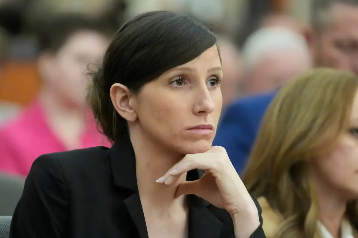 Žena u crnom sakou sa bradom na ruci gleda u daljinu