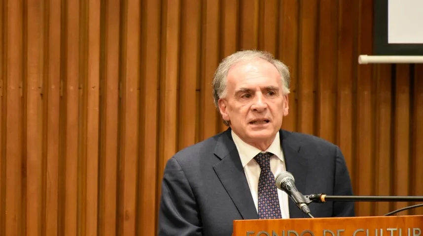 Mudri muškarac u odijelu govori za govornicom sa mikrofonom ispred drvenog zida.