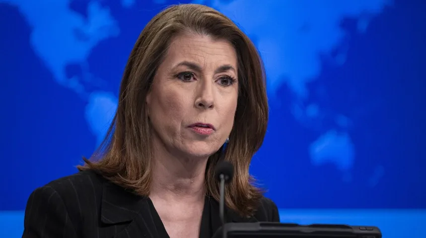 Američka zvaničnica, brineta, govori ispred mikrofona sa mapom svijeta u pozadini.