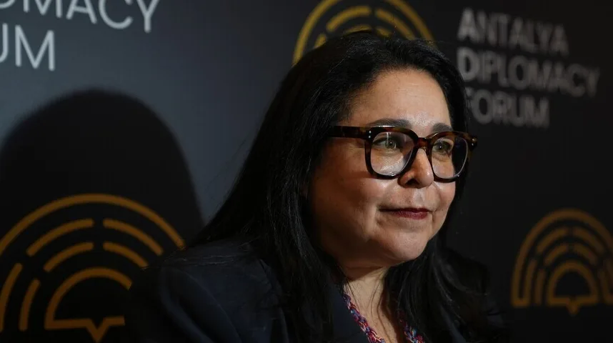 Žena nosi naočare sa smeđim okvirom i tamnu jaknu ispred natpisa 'ANTALYA DIPLOMACY FORUM'.