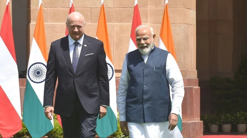 Austrijski izaslanik u crnom odijelu i premijer Indije Narendra Modi u plavom prsluku hodaju ispred zastava Indije i Austrije.