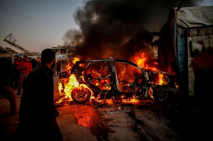 Automobil potpuno u plamenu, gusti crni dim iznad, ljudi promatraju sa strane.