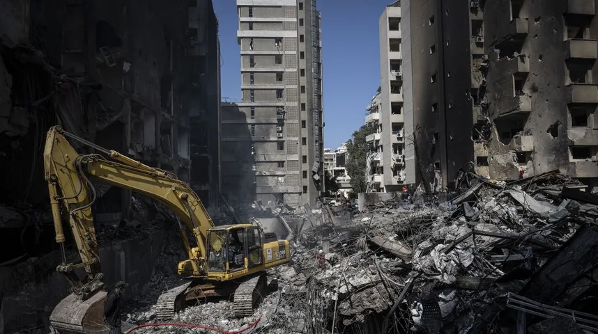 Bager na gradilištu punom ruševina i uništenih zgrada.