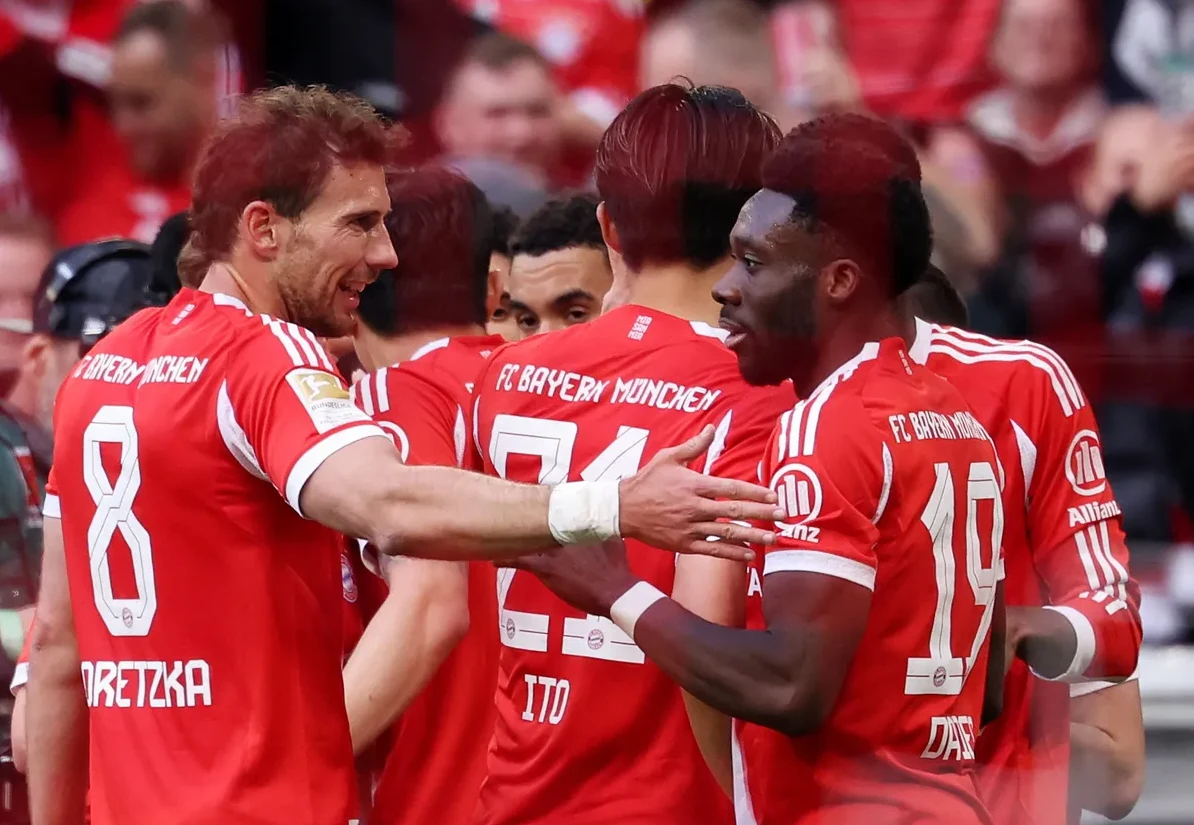 Fudbaleri FC Bajerna iz Minhena u crvenim dresovima slave pogodak na stadionu, vidljivi su brojevi 8 i 19 na dresovima, te prezimena Goretzka i Davies.