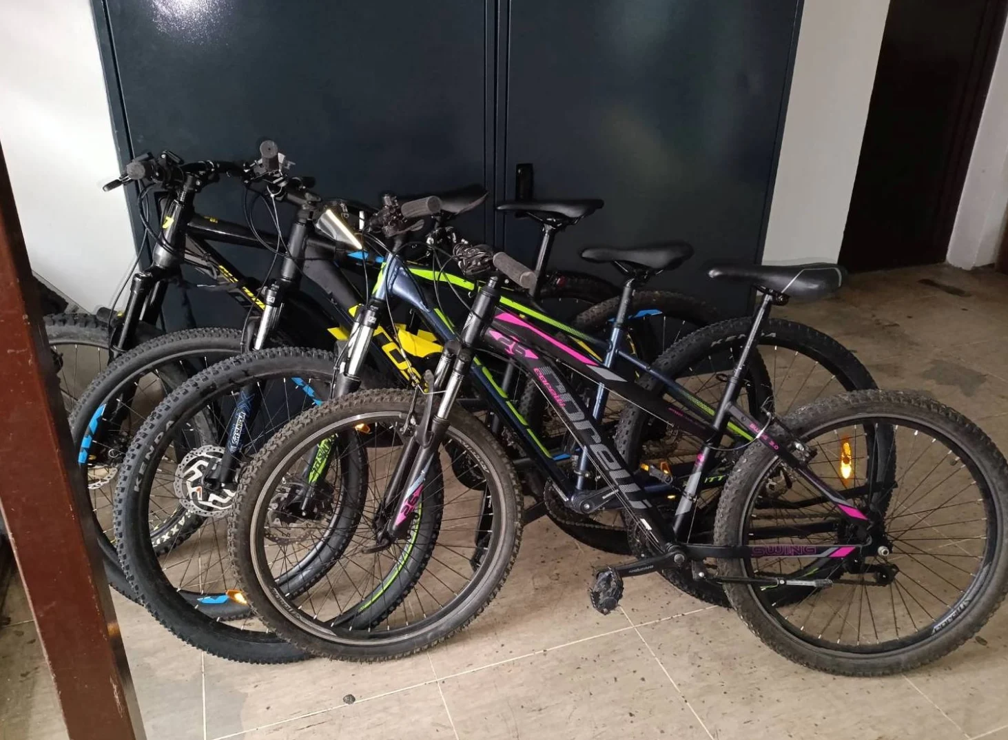 Nekoliko brdskih bicikala složenih uza zid, spremnih za vožnju ili skladištenje.