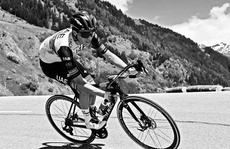 Biciklista vozi uzbrdo u planinama noseći dres UAE tima