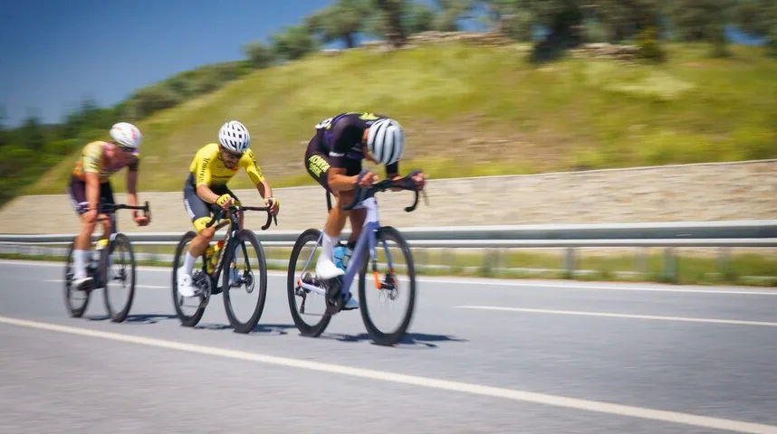 Tri biciklista takmiče se na putu tokom sunčanog dana.
