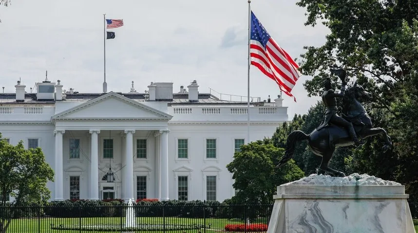 Pogled na Bijelu kuću sa američkom zastavom koja se vijori ispred i statuom jahača na konju u prvom planu.