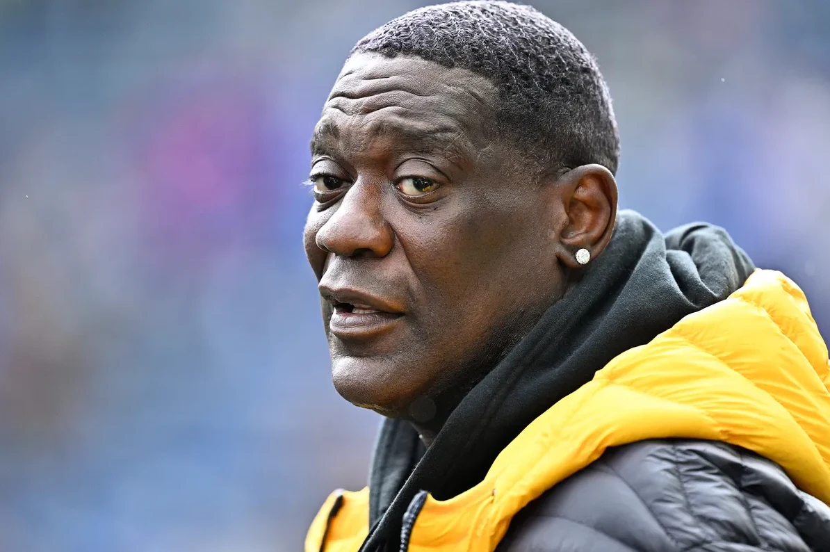 Krupni plan crnog muškarca sa dijamantskom naušnicom u lijevom uhu, obučenog u crnu duksericu i žutu jaknu.