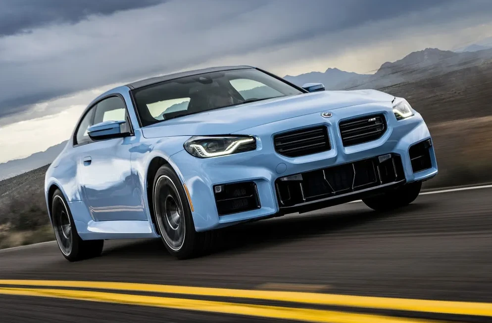 Plavi BMW M2 vozi se autoputem sa planinskim pejzažem u pozadini.