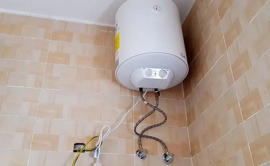 Montirani bojler na struju sa cijevima i termostatom na zidnom kupatilskom zidu.