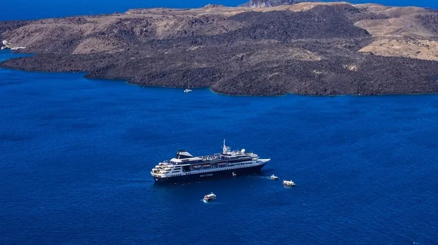 Veliki kruzer i manji brodovi na plavom moru blizu vulkanskog ostrva