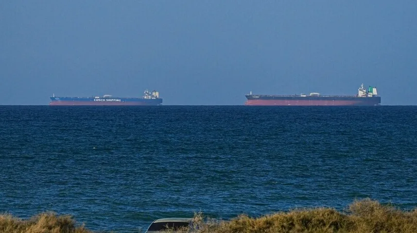 Dva velika teretna broda plove na mirnom plavom moru, pod vedrim nebeskim svodom.