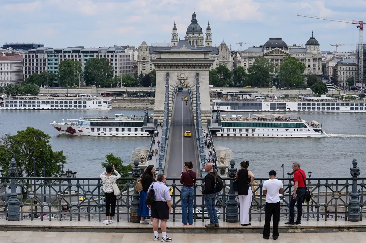Grupa turista posmatra Lančani most u Budimpešti sa kruzerima na Dunavu u pozadini.