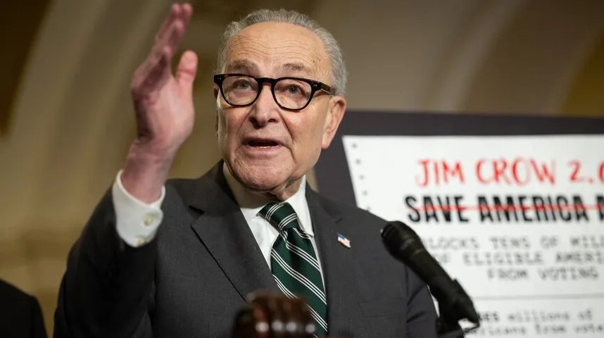 Senatorka Chuck Schumer drži govor sa podignutom rukom, noseći odijelo i zelenu kravatu sa bijelim prugama.