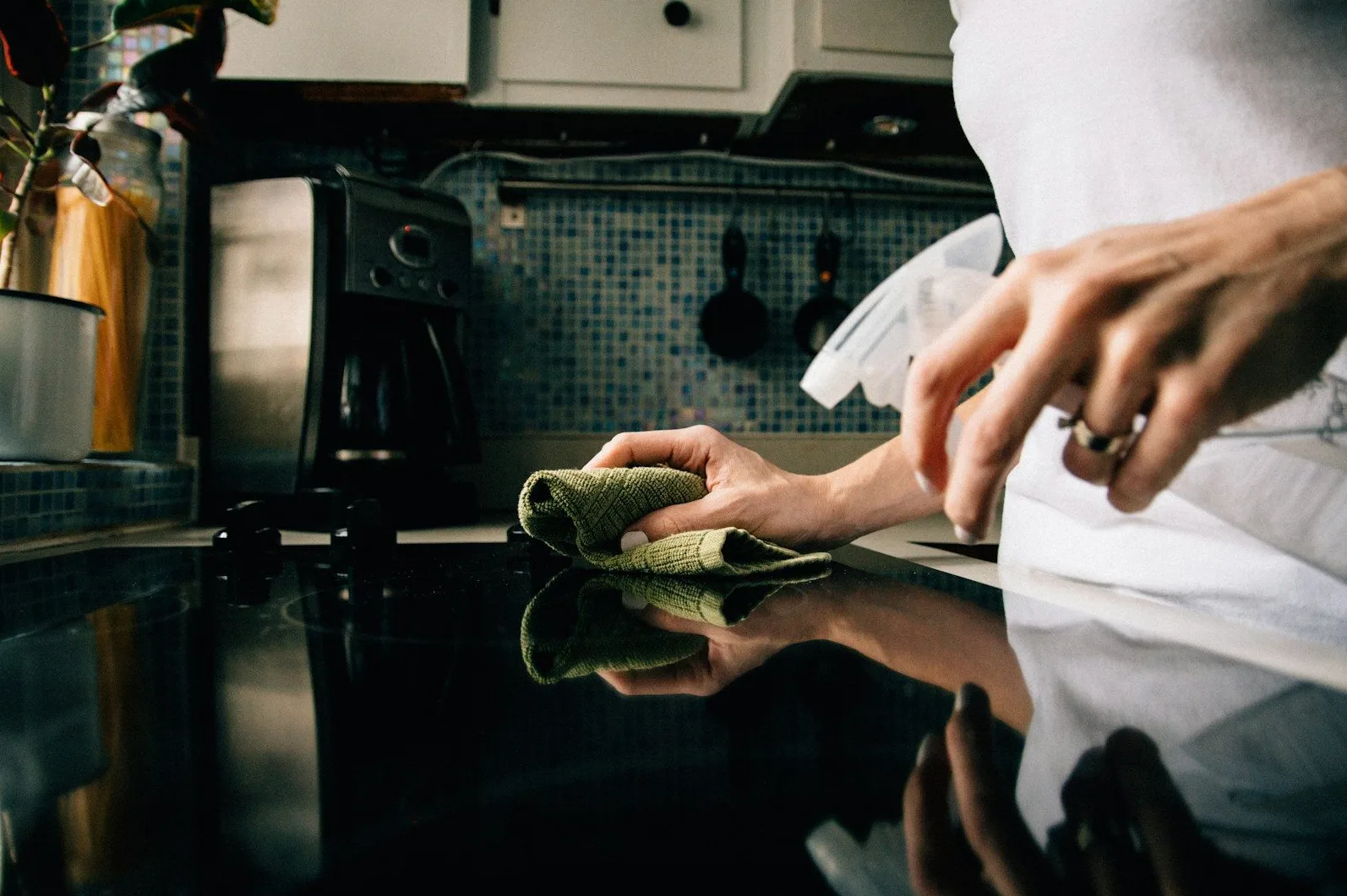 Ruka koja čisti staklenu ploču štednjaka zelenom krpom