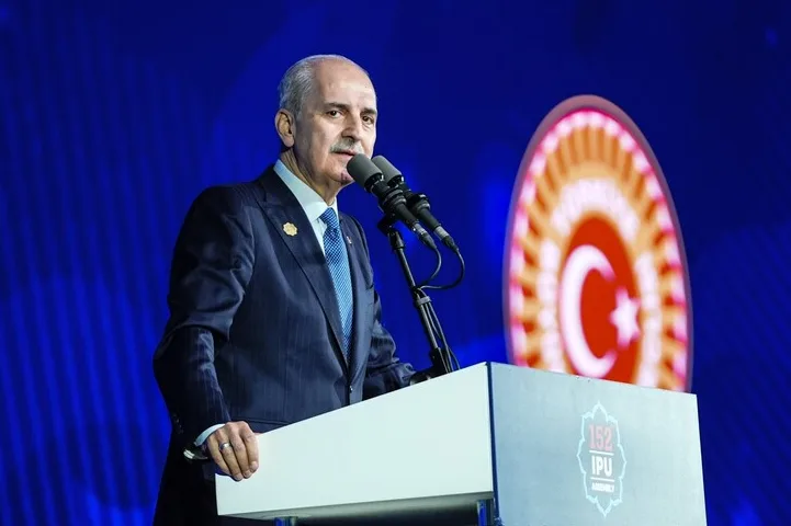 Političar u tamnom odijelu i sa plavom kravatom obraća se sa govornice sa dva mikrofona. Na podijumu se vidi logo "152 IPU ASSEMBLY", a u pozadini je osvijetljeni logo sa turskom zastavom.