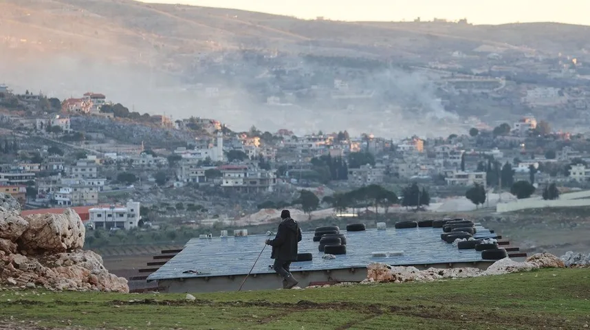 Čovjek sa štapom na krovu objekta, s pogledom na selo u maglovitom jutru.