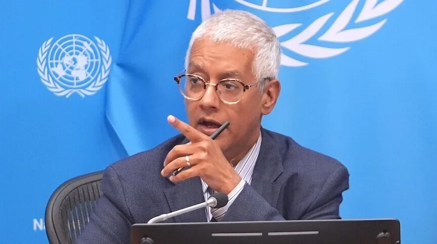 Čovjek sa naočarima i olovkom u ruci ispred plave pozadine sa grbom Ujedinjenih naroda.