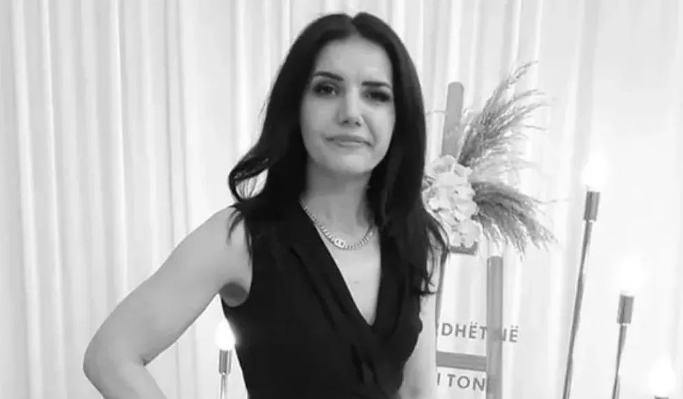 Crno-bijela fotografija žene sa crnom kosom i crnom haljinom koja nosi ogrlicu.