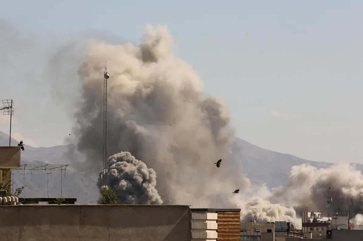 Veliki oblaci dima iznad urbanog područja, sa planinama u pozadini.