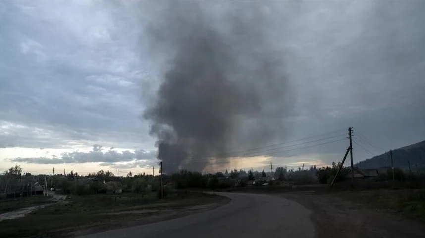 Crni gusti dim suklja u nebo iznad naselja pri zalasku sunca.