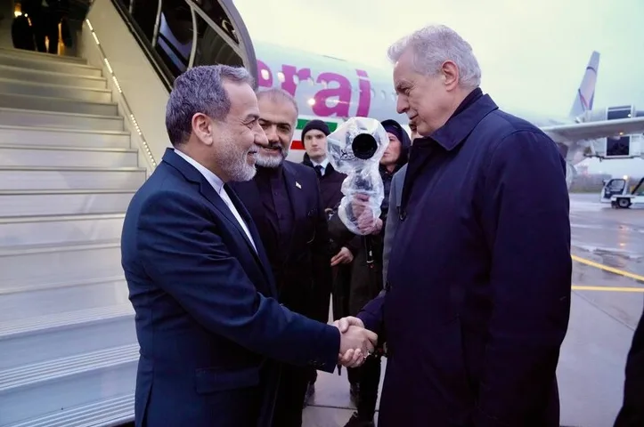 Dvojica muškaraca u odijelima se rukuju ispred stepenica aviona.