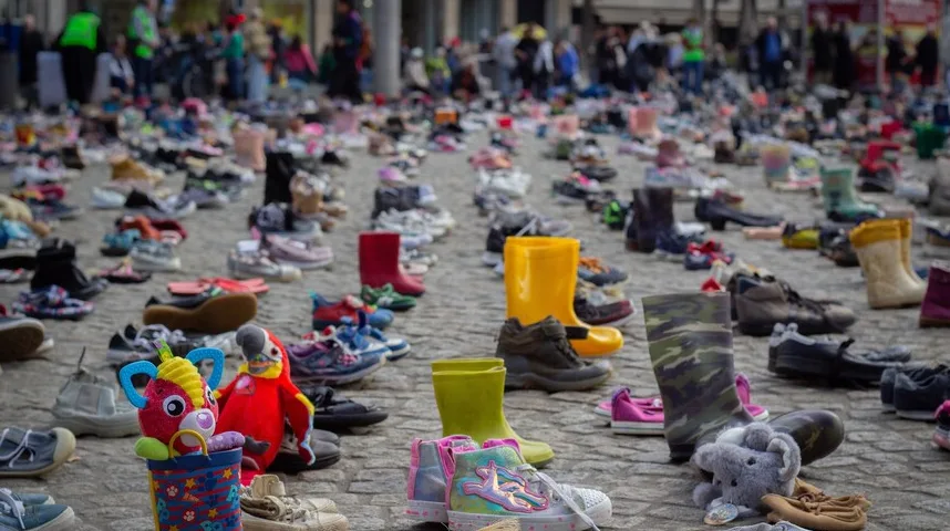 Postavljene dječije cipele na kaldrmisanom trgu, sa nekoliko igračaka u prvom planu.