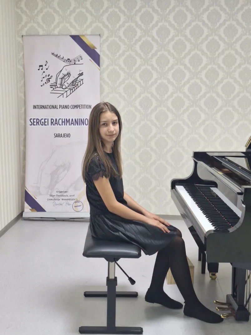 Mlada djevojčica u crnoj haljini sjedi na stolici pred klavirom na takmičenju "Sergei Rachmaninoff" u Sarajevu.