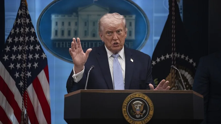 Donald Trump, bivši predsjednik Sjedinjenih Američkih Država, stoji iza podijuma sa podignutom desnom rukom i izgovara govor, s američkom zastavom i logom Bijele kuće u pozadini.