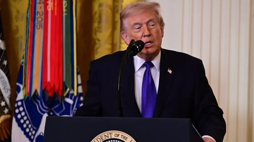 Donald Trump u crnom odijelu i ljubičastoj kravati govori za govornicu.