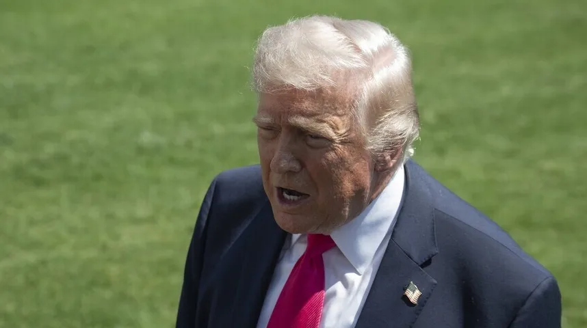 Donald Trump u tamnom odijelu, bijeloj košulji i roze kravati, sa blago otvorenim ustima, stoji napolju na zelenoj travi.