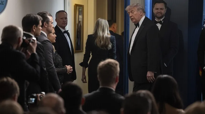 Donald Trump u crnom smokingu sa leptir mašnom stoji pored supruge Melanije Trump, koja nosi elegantnu crnu haljinu, dok ih prate agenti i novinari.