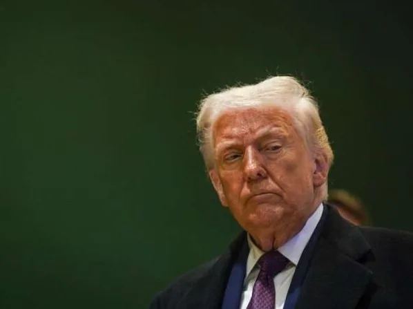 Donald Trump u tamnom odijelu i ljubičastoj kravati, s ozbiljnim izrazom lica.