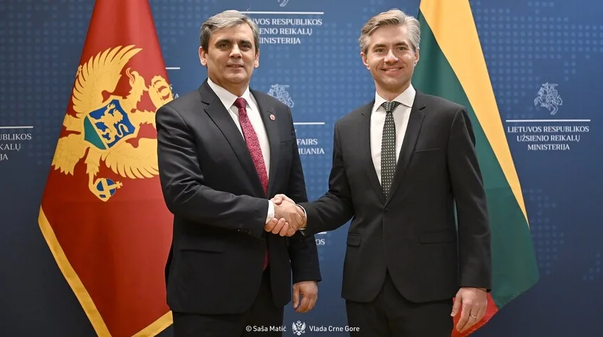 Dvije zastave, Crne Gore i Litvanije, stoje jedna pored druge dok se dva muškarca u odijelima rukuju.