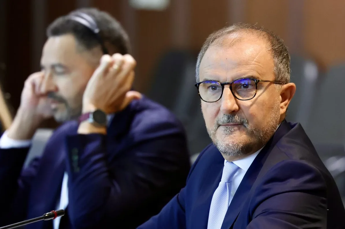 Dva muškarca u odijelima na sastanku, jedan nosi slušalice