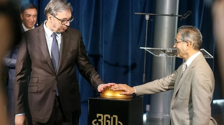 Dva gospodina u odijelima zajednički pritiskaju veliko zlatno dugme na crnom postolju.