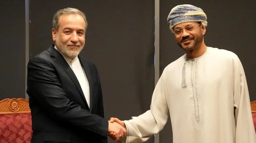 Dva muškarca, jedan u crnom odijelu i bijeloj košulji, a drugi u tradicionalnoj bijeloj odjeći i turbanu, rukuju se