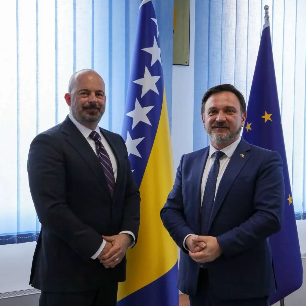 Dvojica muškaraca u odijelima stoje ispred zastava Bosne i Hercegovine i Evropske unije.
